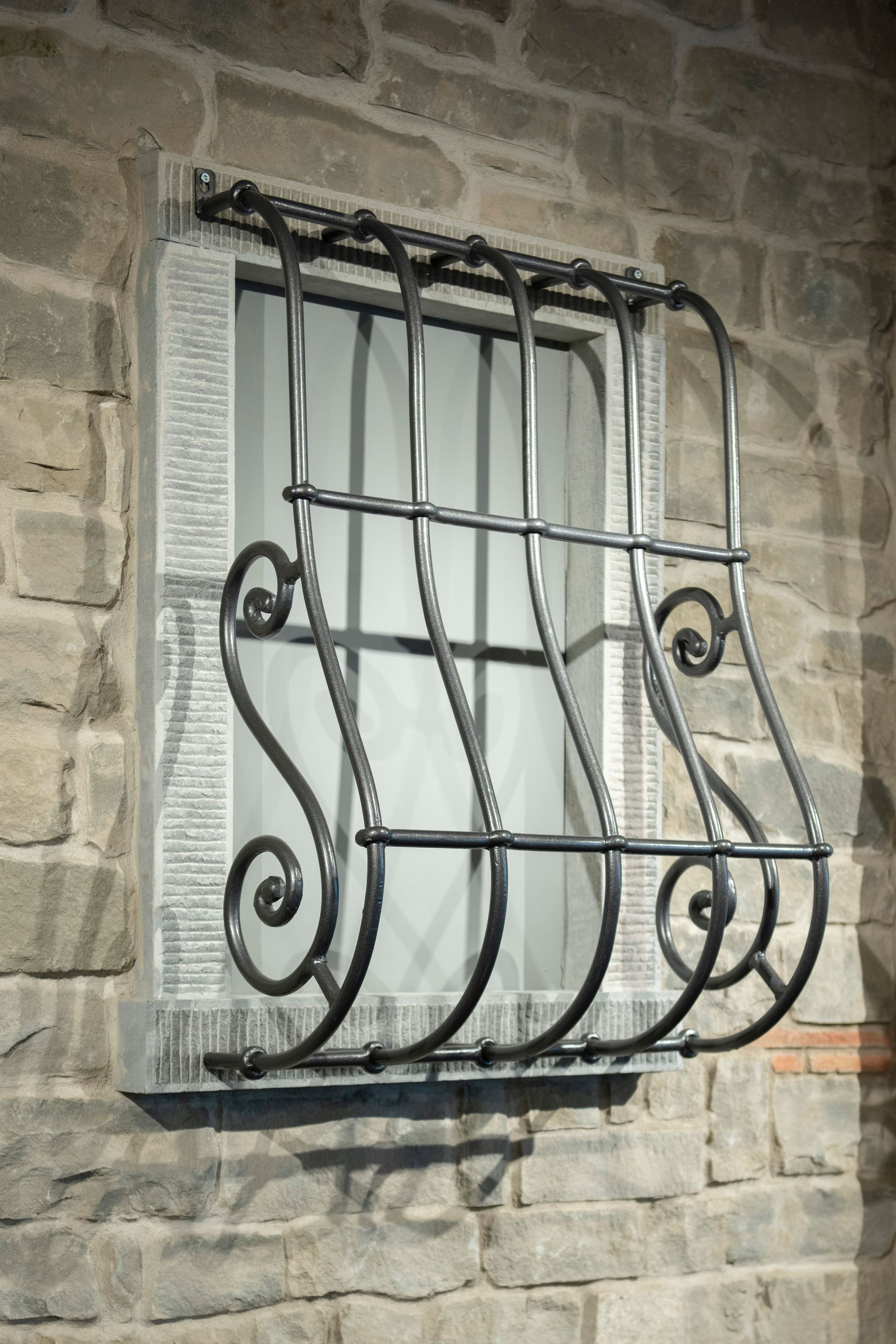 Finestra con inferriate decorative in ferro battuto incastonate in un muro di pietra.