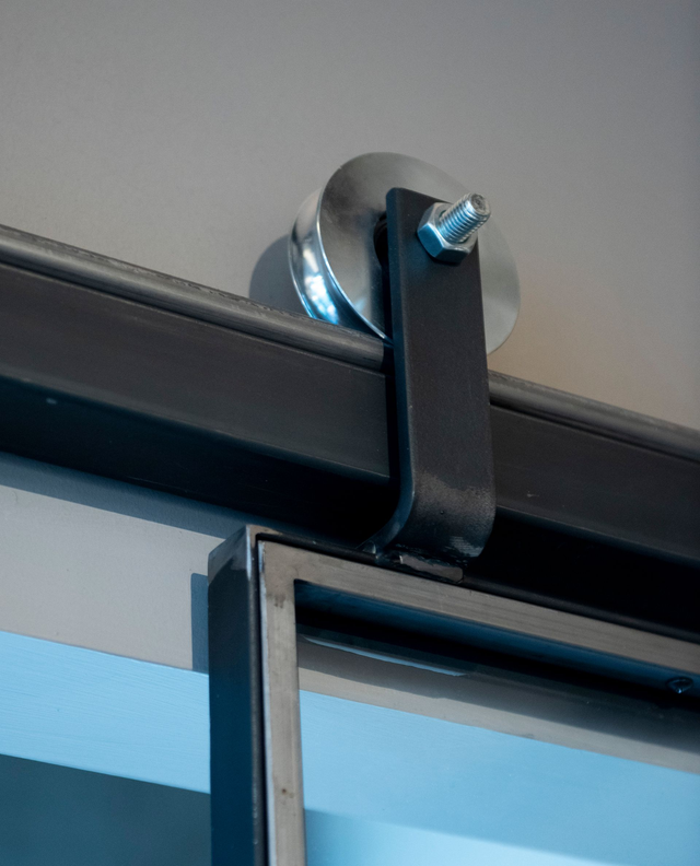 Ferramenta per porte da fienile: binario in metallo nero con rullo fissato al telaio della porta, montato sul soffitto.