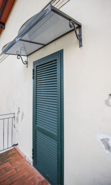 Porta verde con persiana sotto una tenda trasparente, su una parete in stucco di colore chiaro.