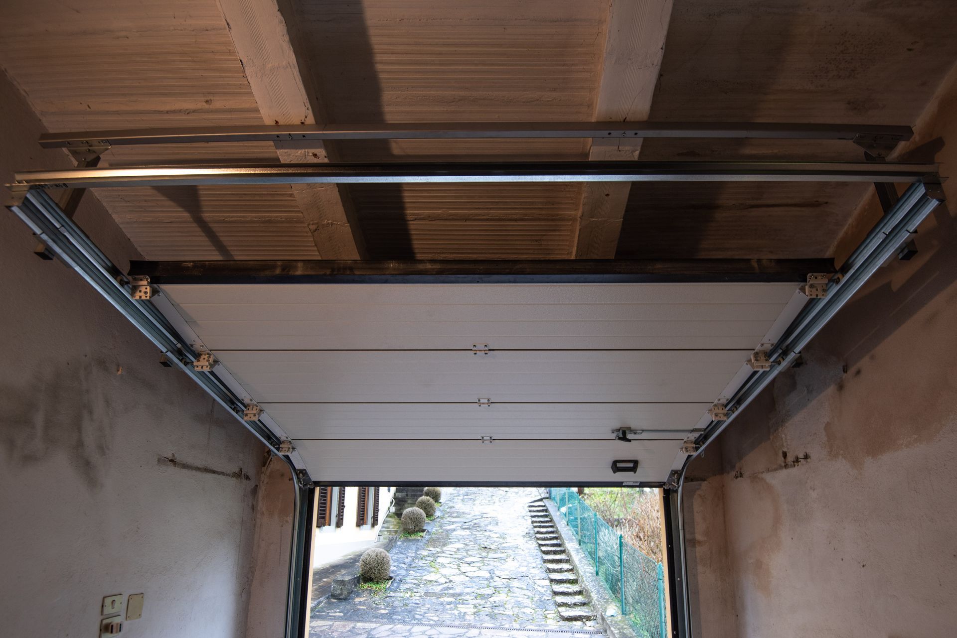 Porta del garage: pannelli bianchi, posizione aperta, montata all'interno di un garage. Vista verso i gradini esterni.