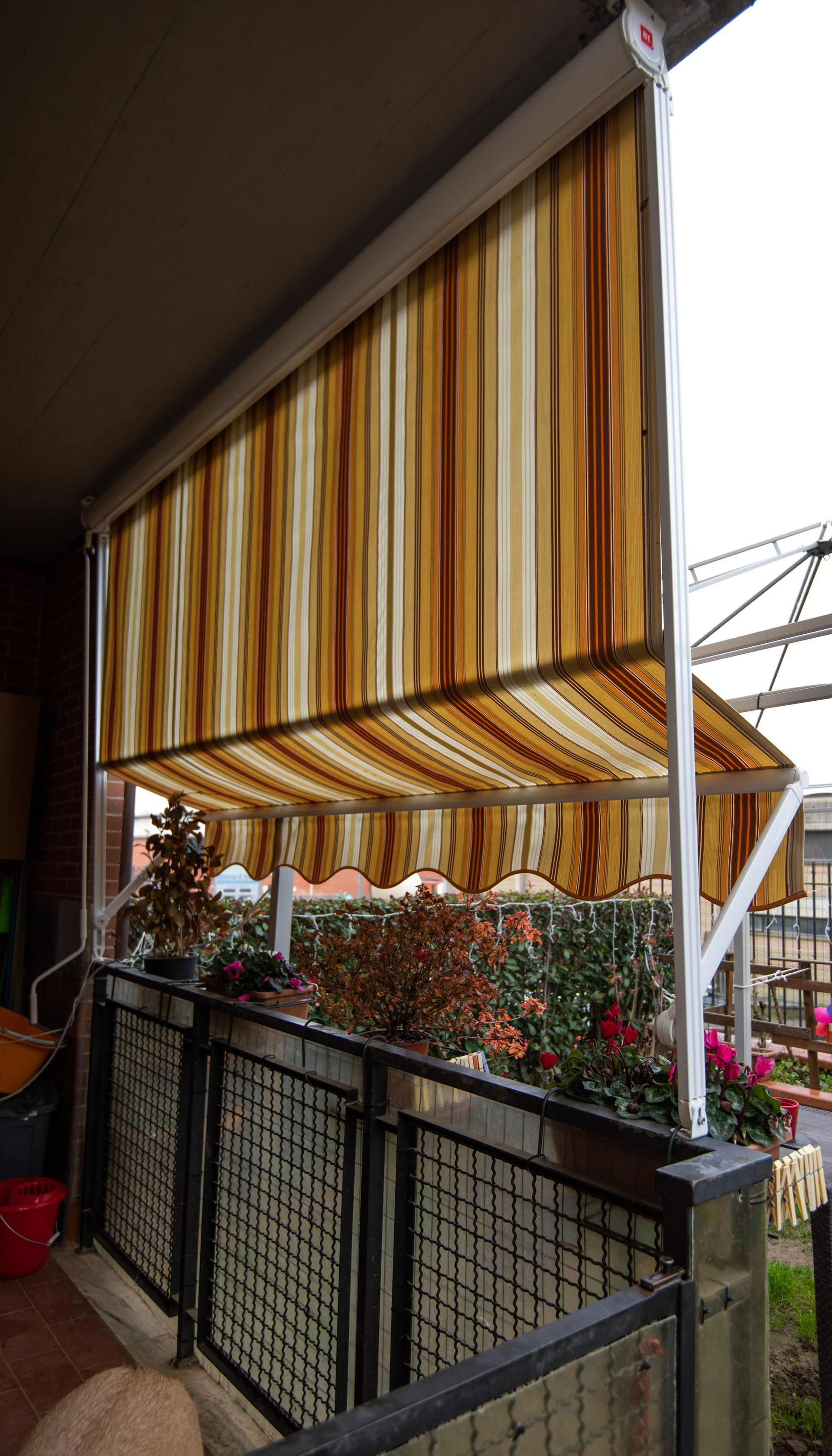 Una tenda a strisce si estende su un balcone con ringhiera in metallo e fioriere.