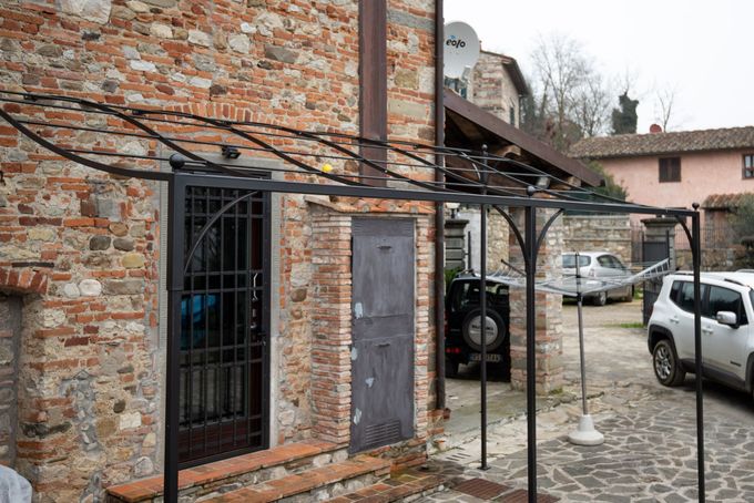 Pergola in metallo nero sopra le porte di un edificio in mattoni, con auto parcheggiate nelle vicinanze.