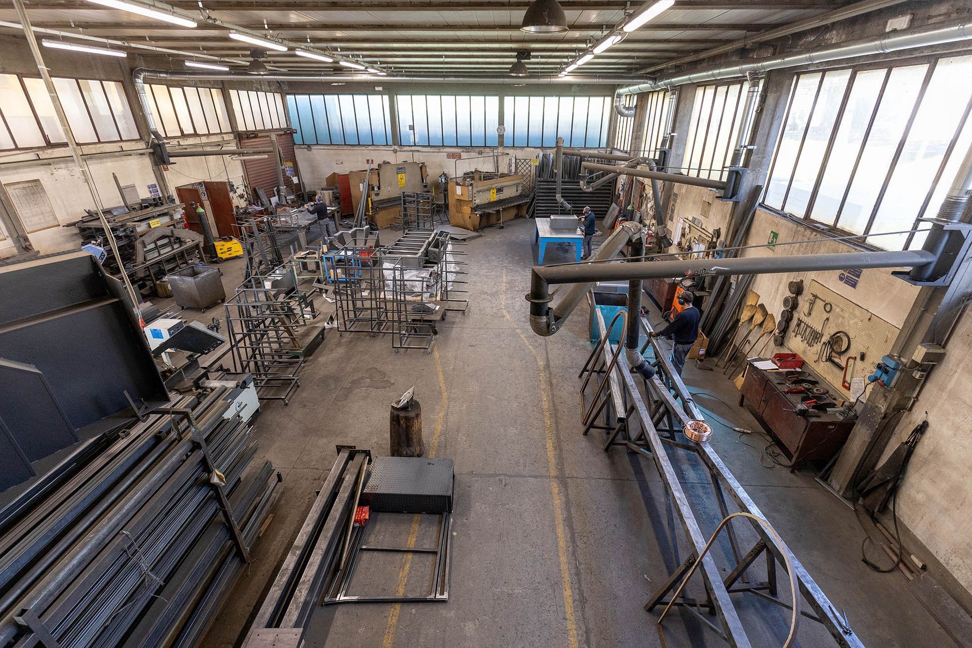 Interno di un'officina con attrezzature e utensili per la lavorazione dei metalli; una persona lavora vicino a un apparecchio di saldatura.