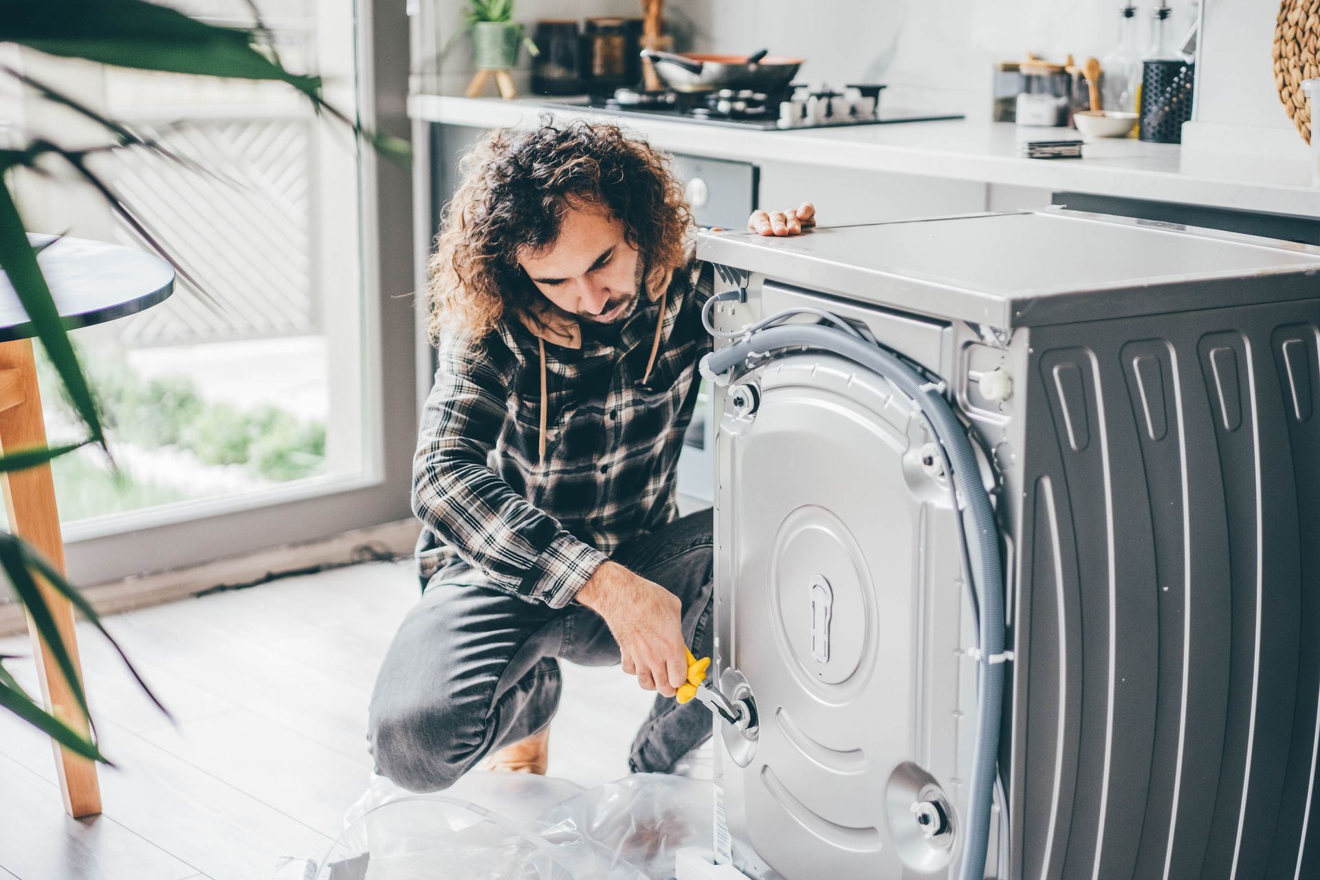 A man is fixing a washing machine in a kitchen.