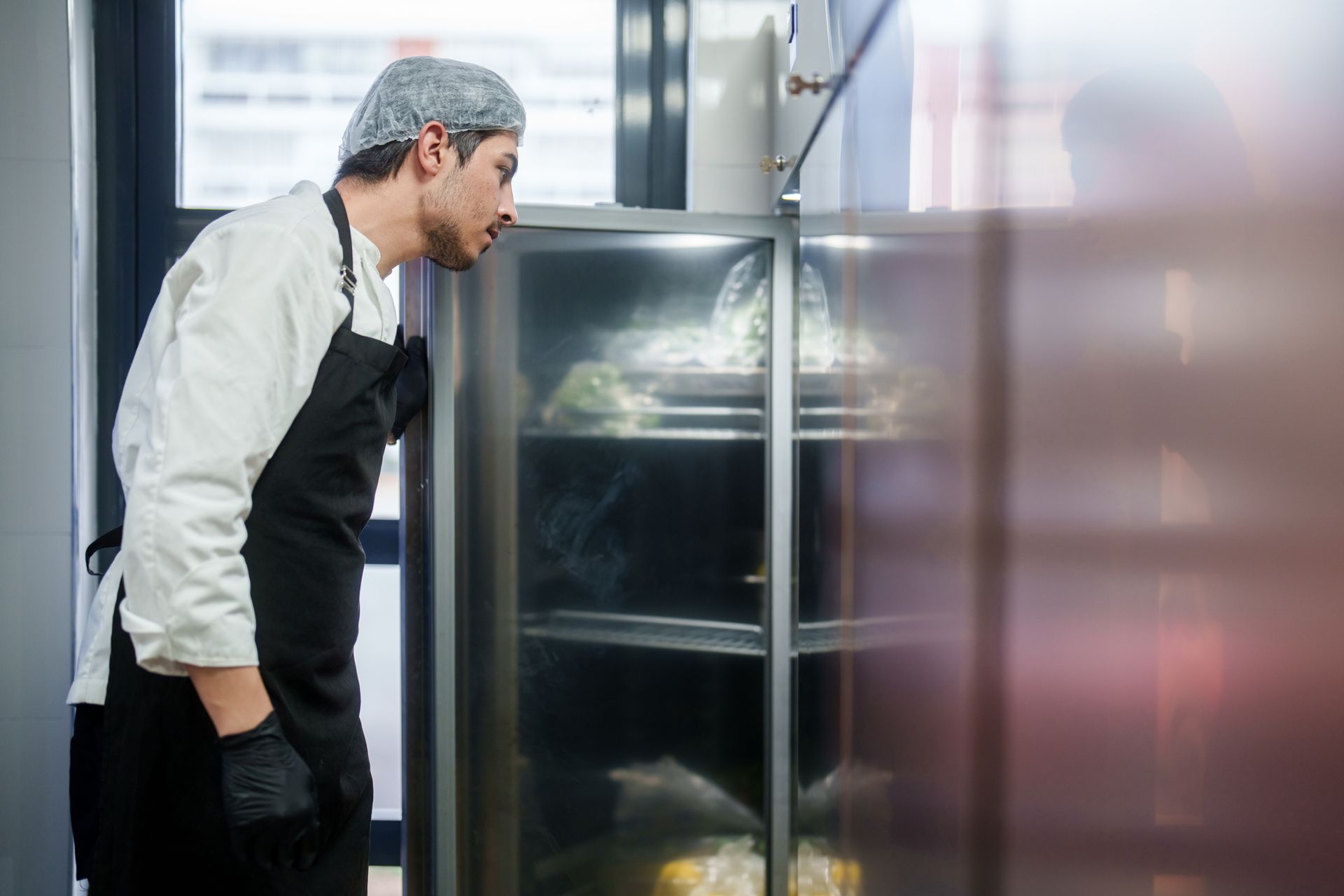 A chef is looking into a refrigerator filled with food.