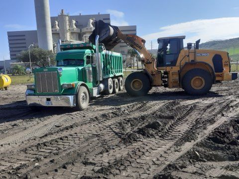 A dump truck is being loaded with dirt by a bulldozer
