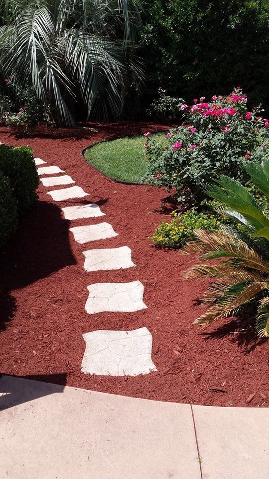 Stepping stones path through red mulch garden, with green plants and pink flowers.