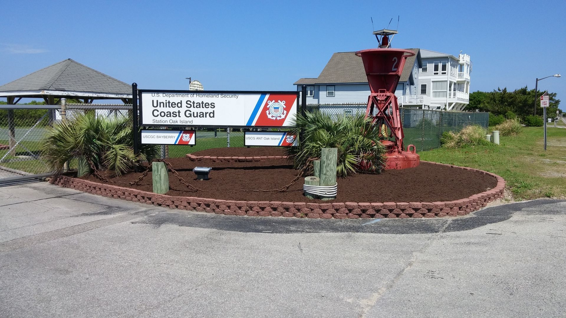 Sign for US Coast Guard station with a red buoy in a garden bed.