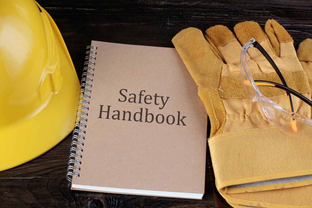 A Safety Handbook Is Next To A Hard Hat And Gloves — Canary North Pty Ltd In Annandale, QLD