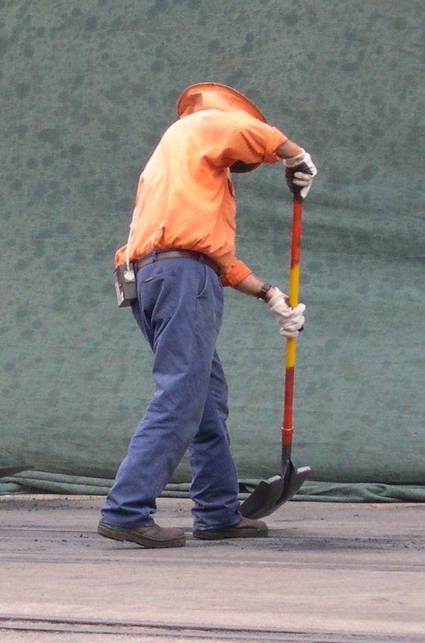 A Man In An Orange Shirt And Blue Pants Is Holding A Shovel — Canary North Pty Ltd In Annandale, QLD