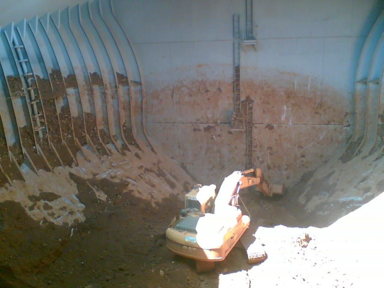 A Small Yellow Excavator Is Sitting In The Dirt Next To A Large White Wall — Canary North Pty Ltd In Annandale, QLD