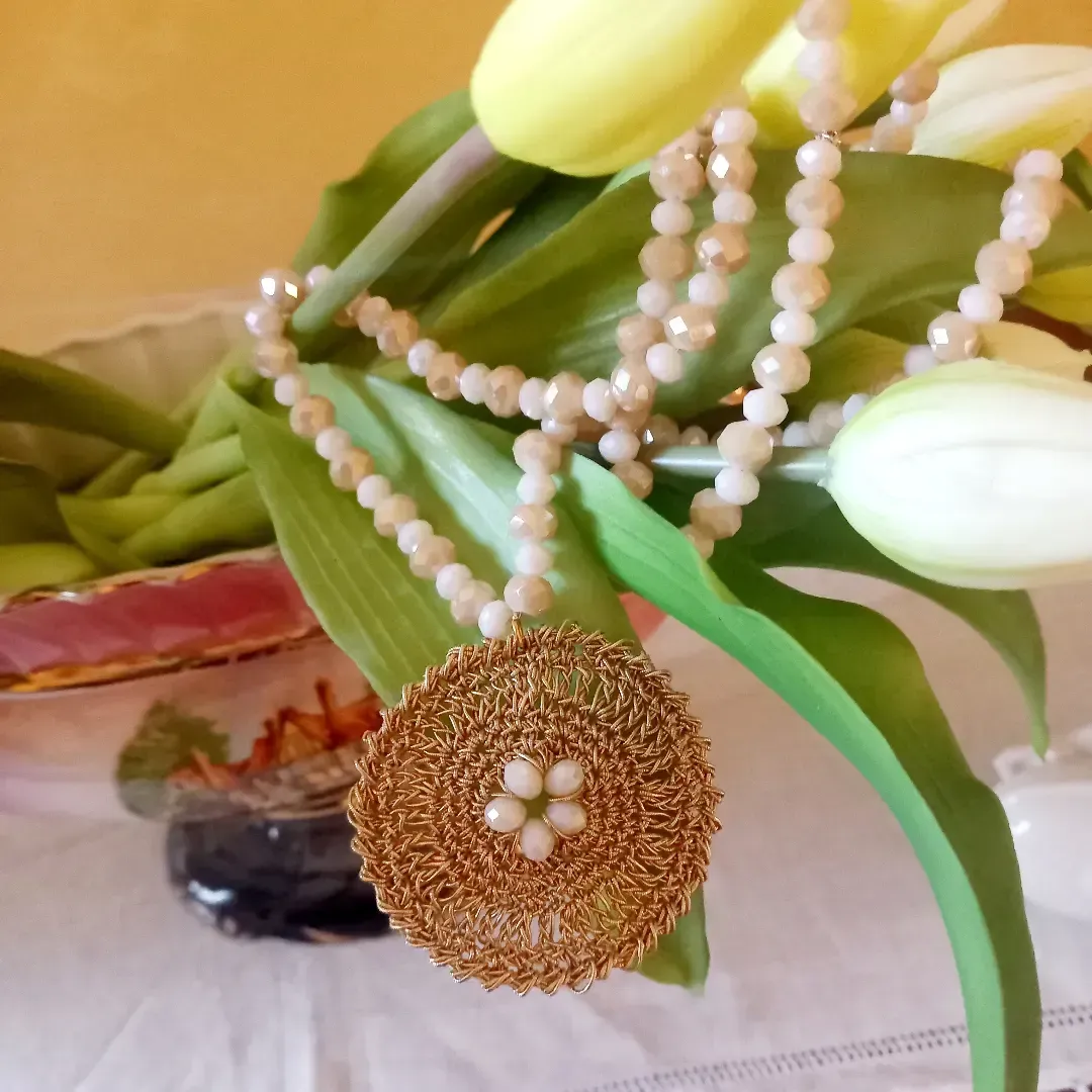 Primo piano di una composizione floreale con tulipani gialli e bianchi, foglie verdi e ghirlande di perline simili a perle.