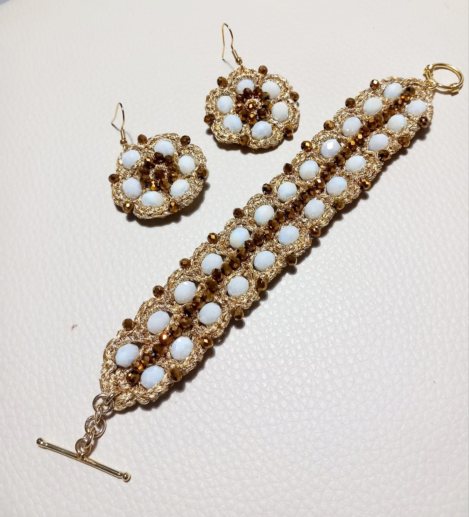 Bracciale in oro e perle bianche con orecchini circolari abbinati su sfondo chiaro.
