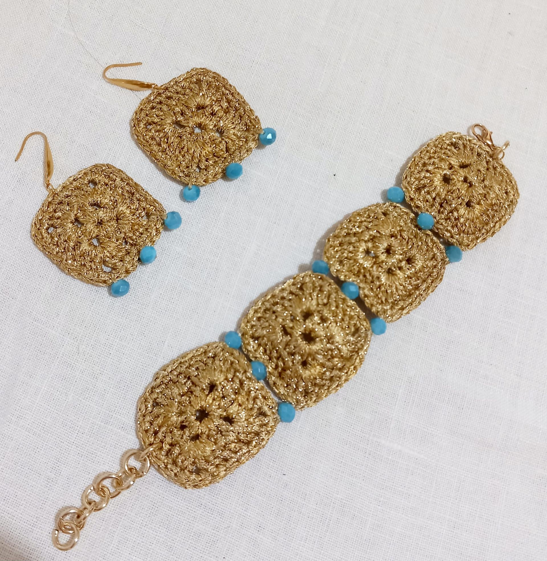 Bracciale con perline dorate e orecchini abbinati con dettagli turchesi su sfondo bianco.