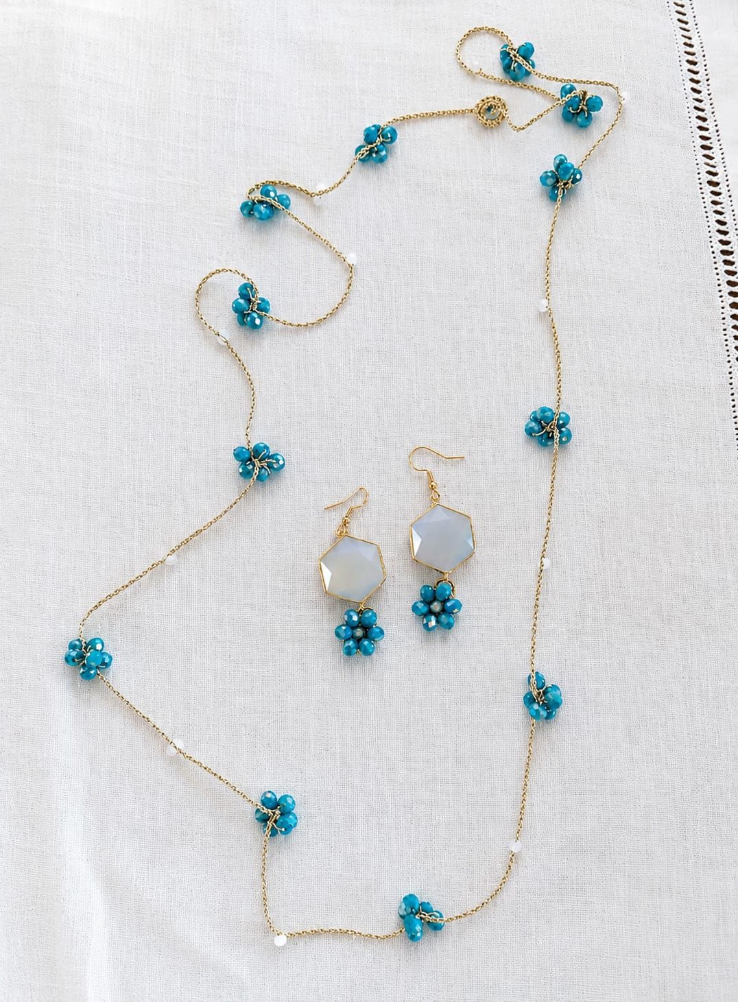 Set di gioielli con fiori turchesi: collana, bracciale e orecchini pendenti su sfondo bianco.