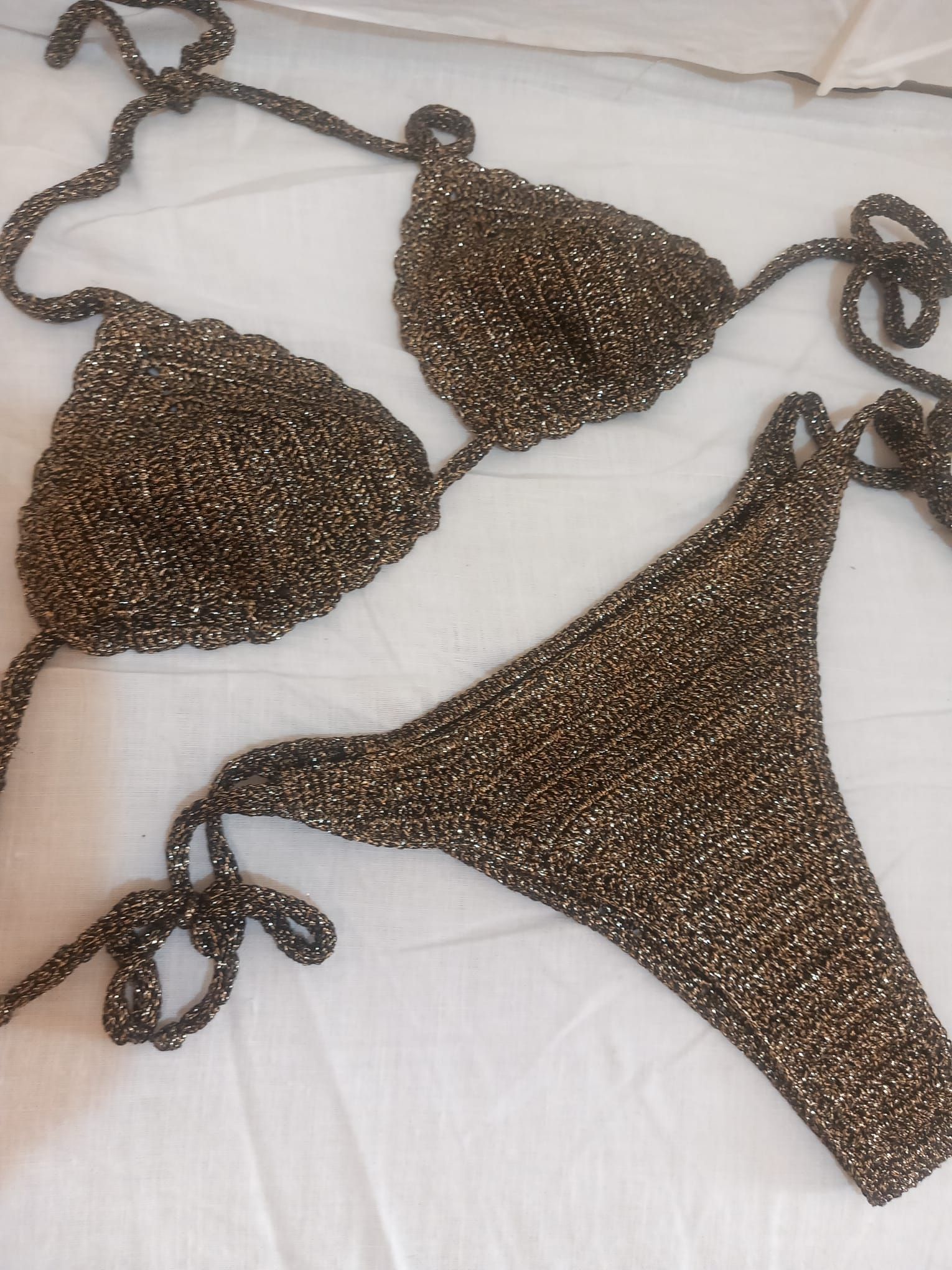Bikini a triangolo marrone con perline, adagiato su una coperta bianca.
