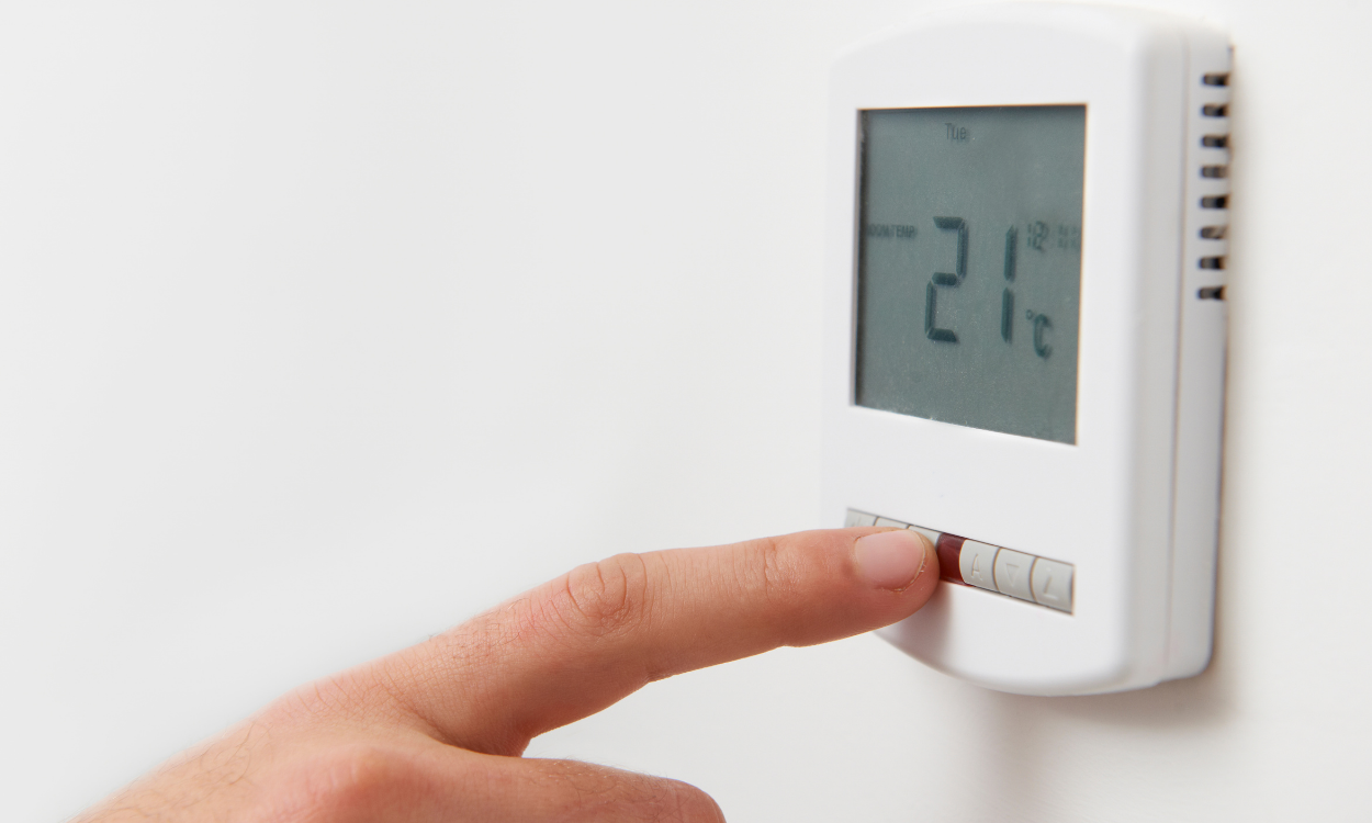Finger pressing a wall thermostat showing 21°C