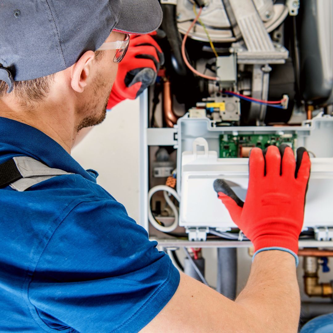 A person in a blue shirt and red safety gloves repairing the internal components of a wall-mounted gas boiler.