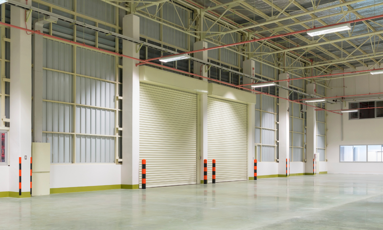 Empty industrial warehouse interior with roll-up doors, bright overhead lighting.