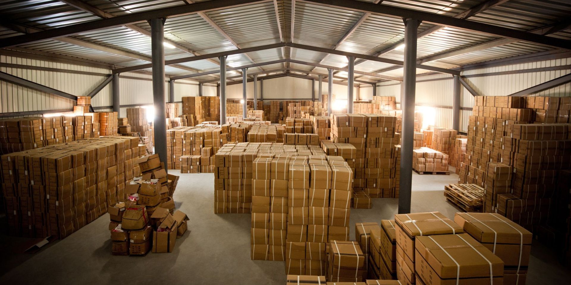 Warehouse filled with stacked cardboard boxes and pallets under a metal roof