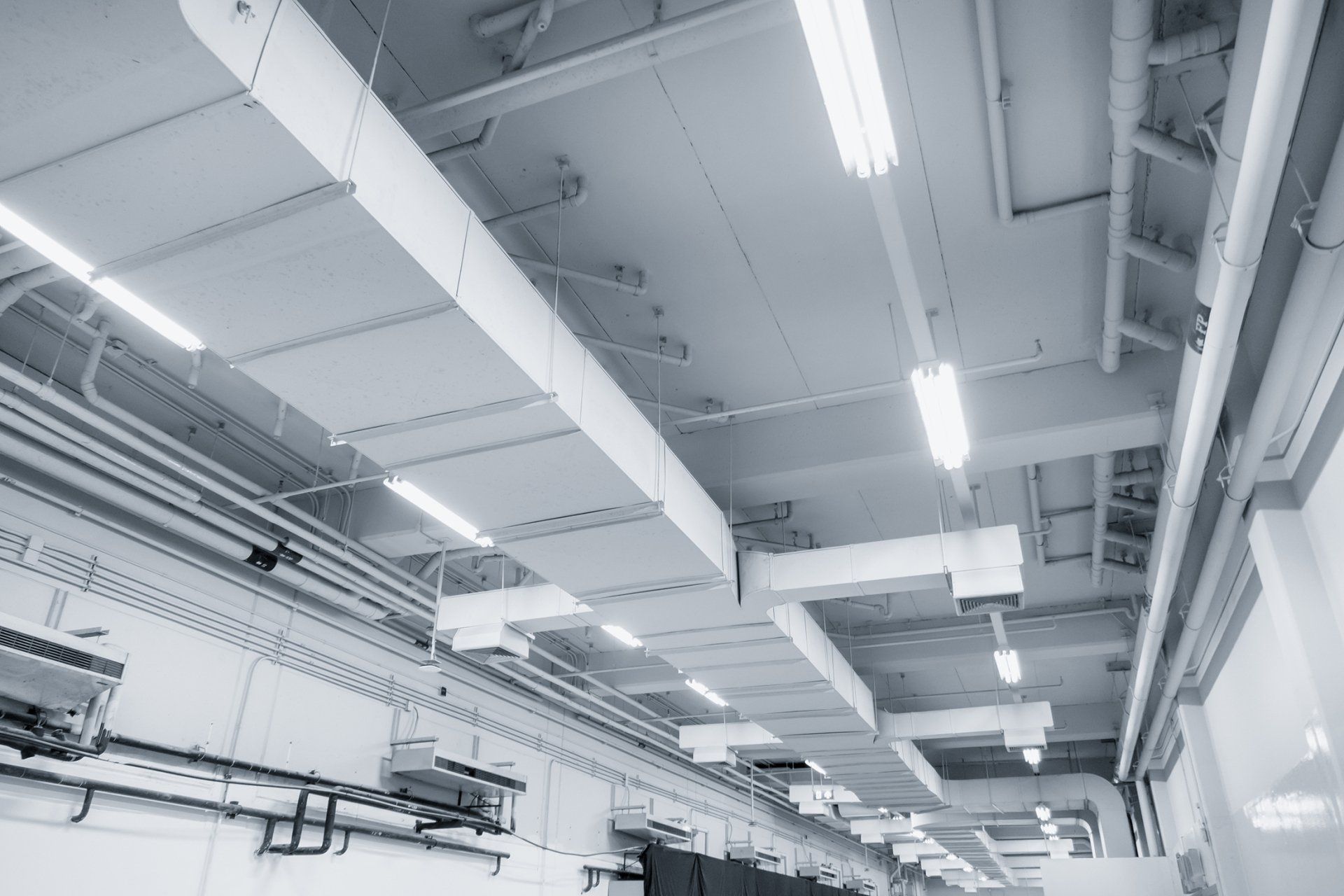 a black and white photo of a factory heating solutions for a warehouse with a lot of pipes hanging from the ceiling .