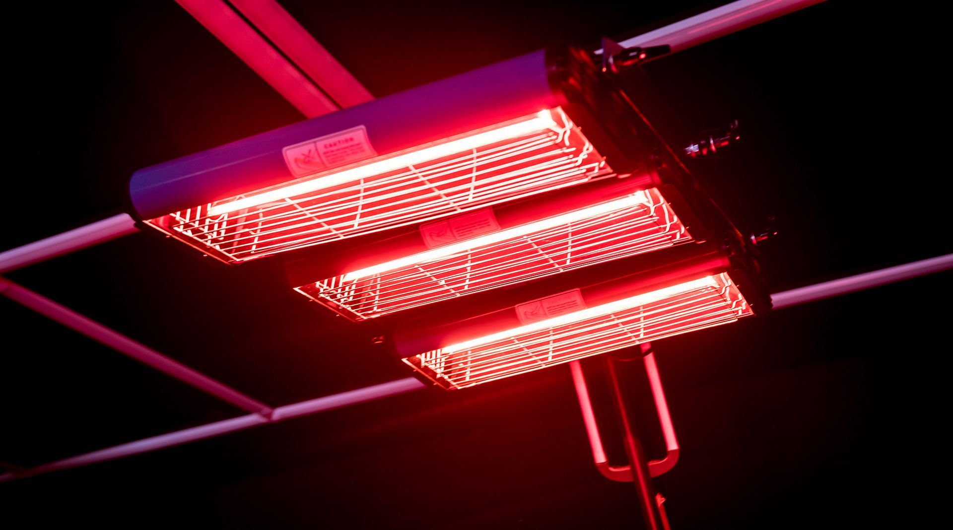 Red infared heaters is hanging from the ceiling in a dark room.