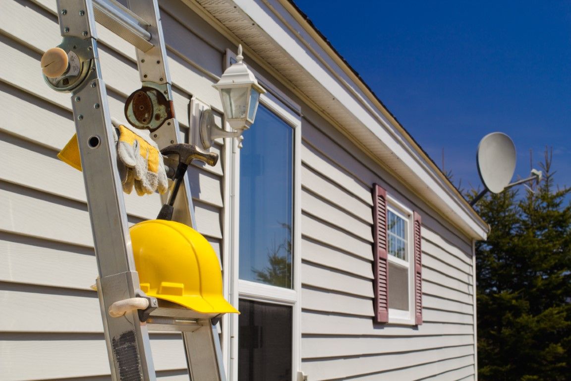 Ladder with hard hat and tools resting against a home's vinyl siding during a repair
