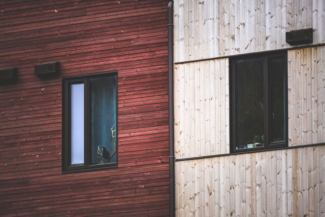 Close-up of red-brown and natural wood siding panels meeting at a corner, with black window frames and exterior vents
