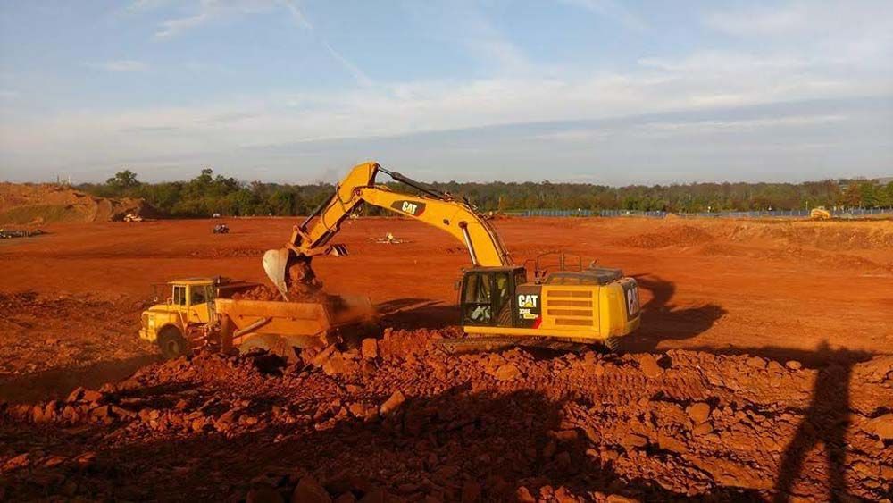 Yellow excavator digging red dirt at a construction site under a clear sky.
