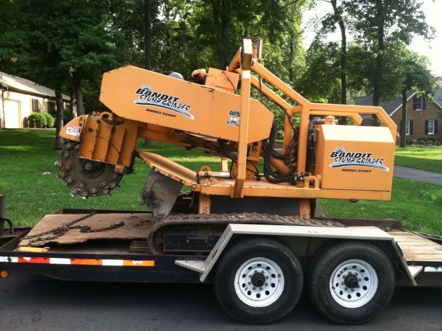 Orange wood chipper on a flatbed trailer outdoors in a grassy yard.