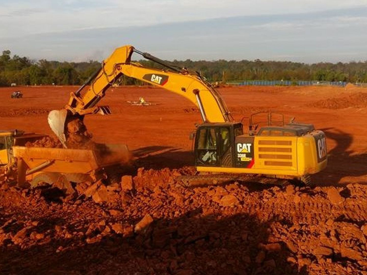 Yellow CAT excavator digging red dirt at a construction site under a clear sky.