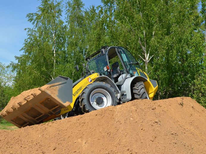 Yellow front loader dumping dirt on a sandy mound with green trees in the background