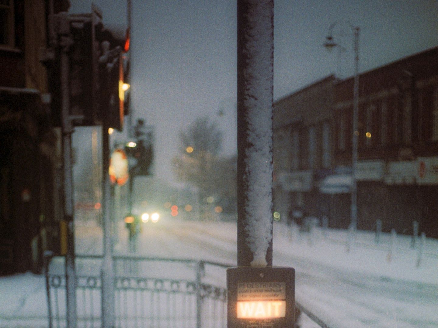 Snowy city street at dusk with blurred lights and a glowing storefront sign.