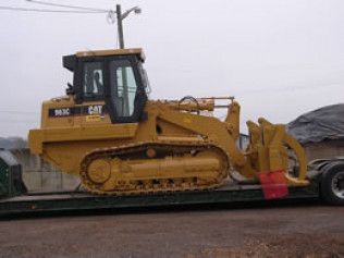 Yellow CAT bulldozer on a flatbed trailer in a muddy lot under a gray sky