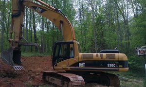 Yellow CAT excavator working in a wooded area with dirt and trees