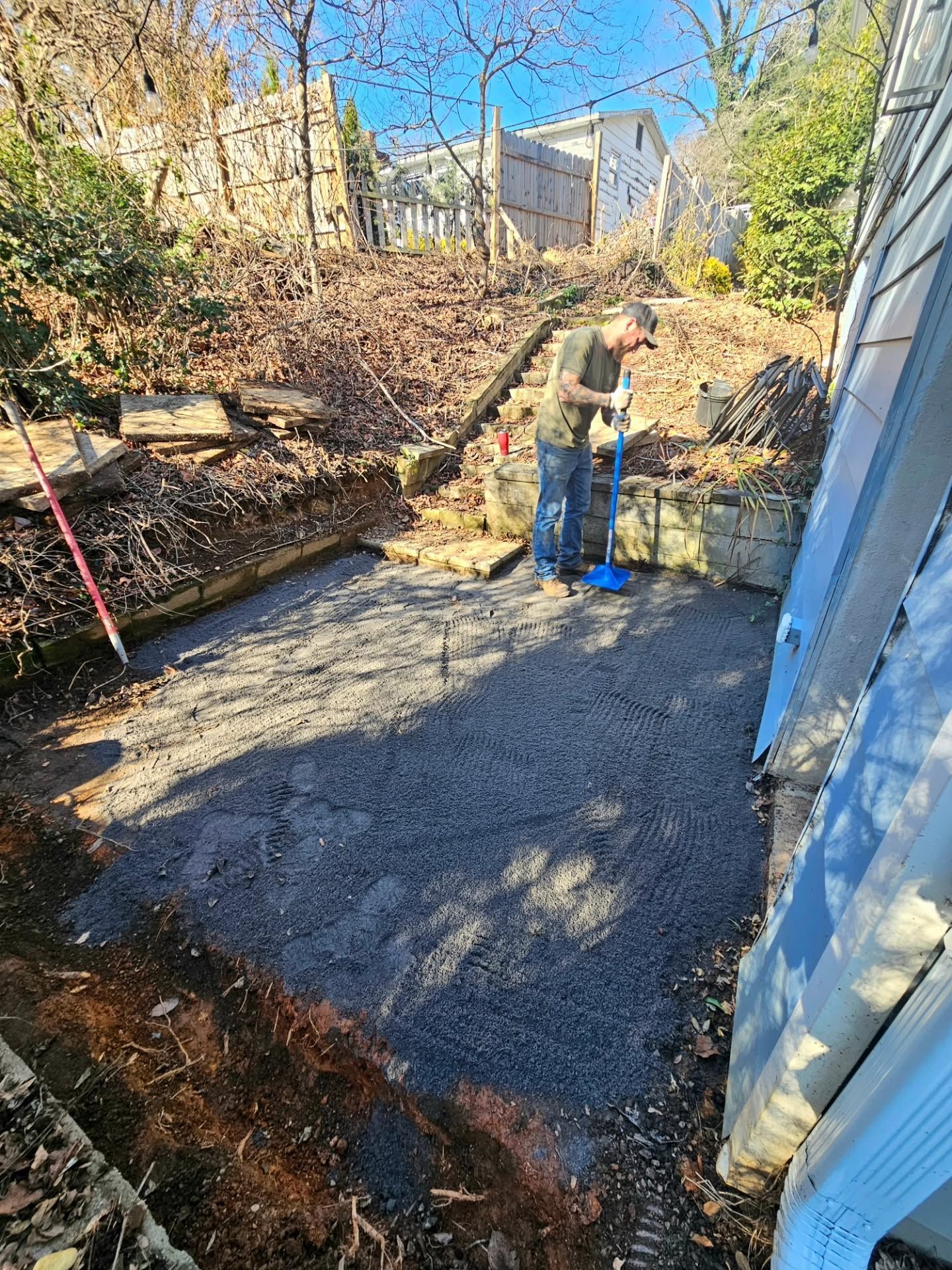 Person working on a concrete foundation in a backyard with tools and plywood forms