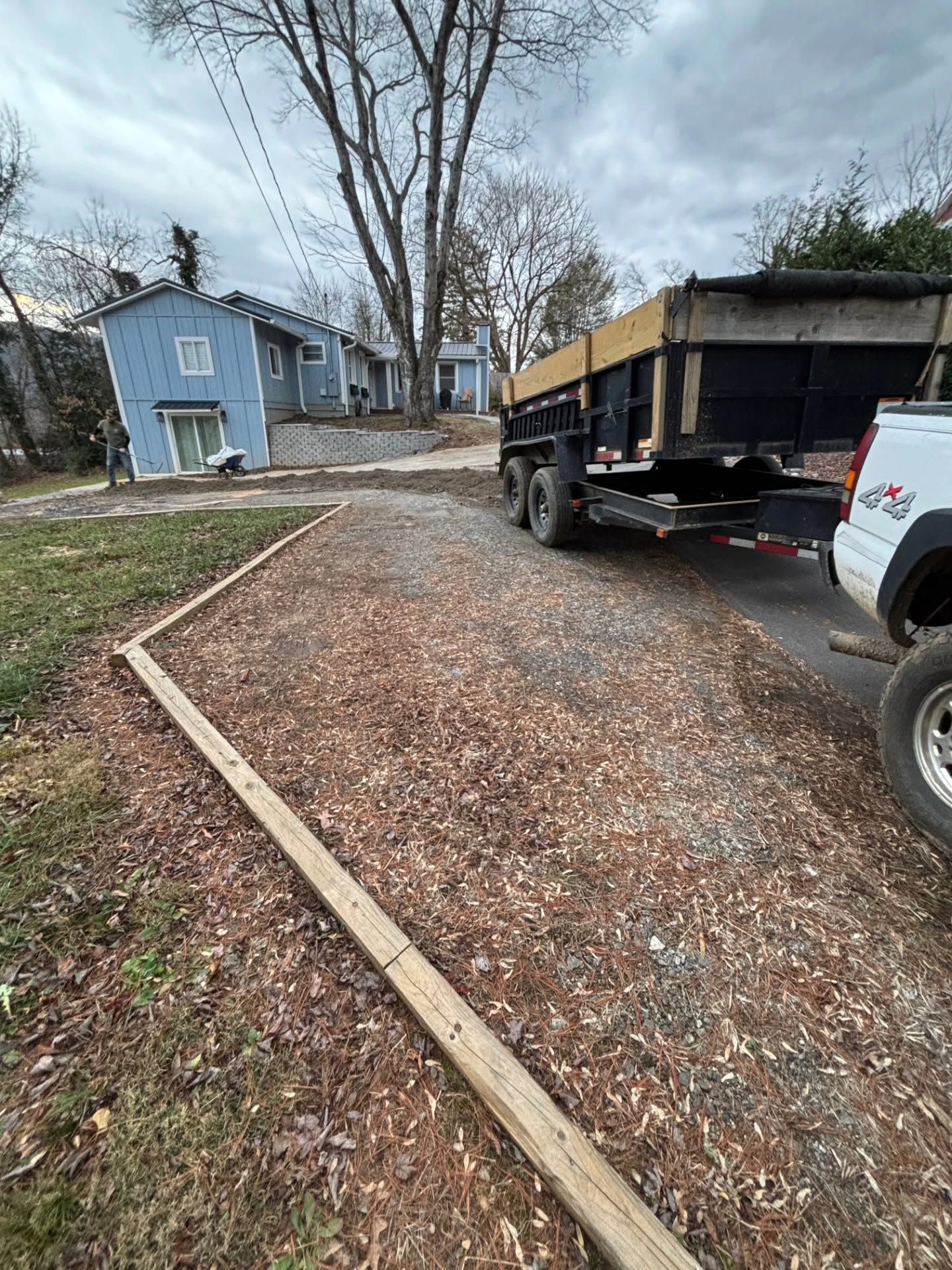 Gravel driveway with a black dump truck beside a blue house on an overcast day