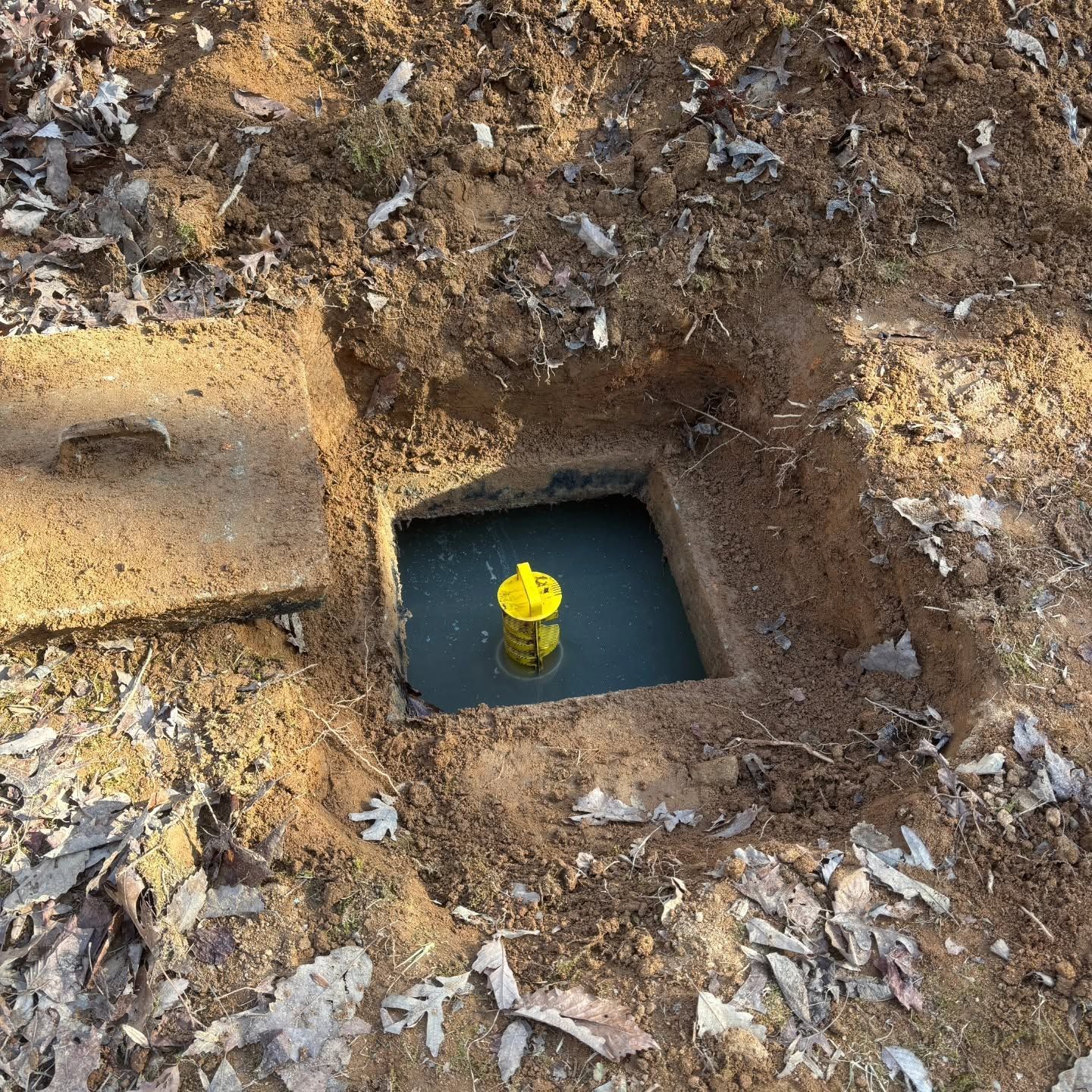 Yellow valve in a square utility box set in muddy ground with debris around it