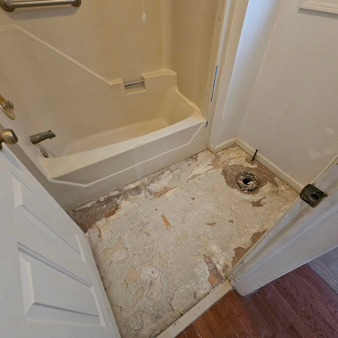 Bathroom with tub and toilet removed, exposing a rough subfloor and drain opening.