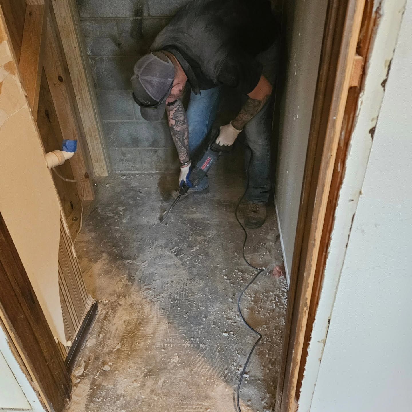 Worker using a power tool to cut concrete in a narrow hallway, with dust on the floor