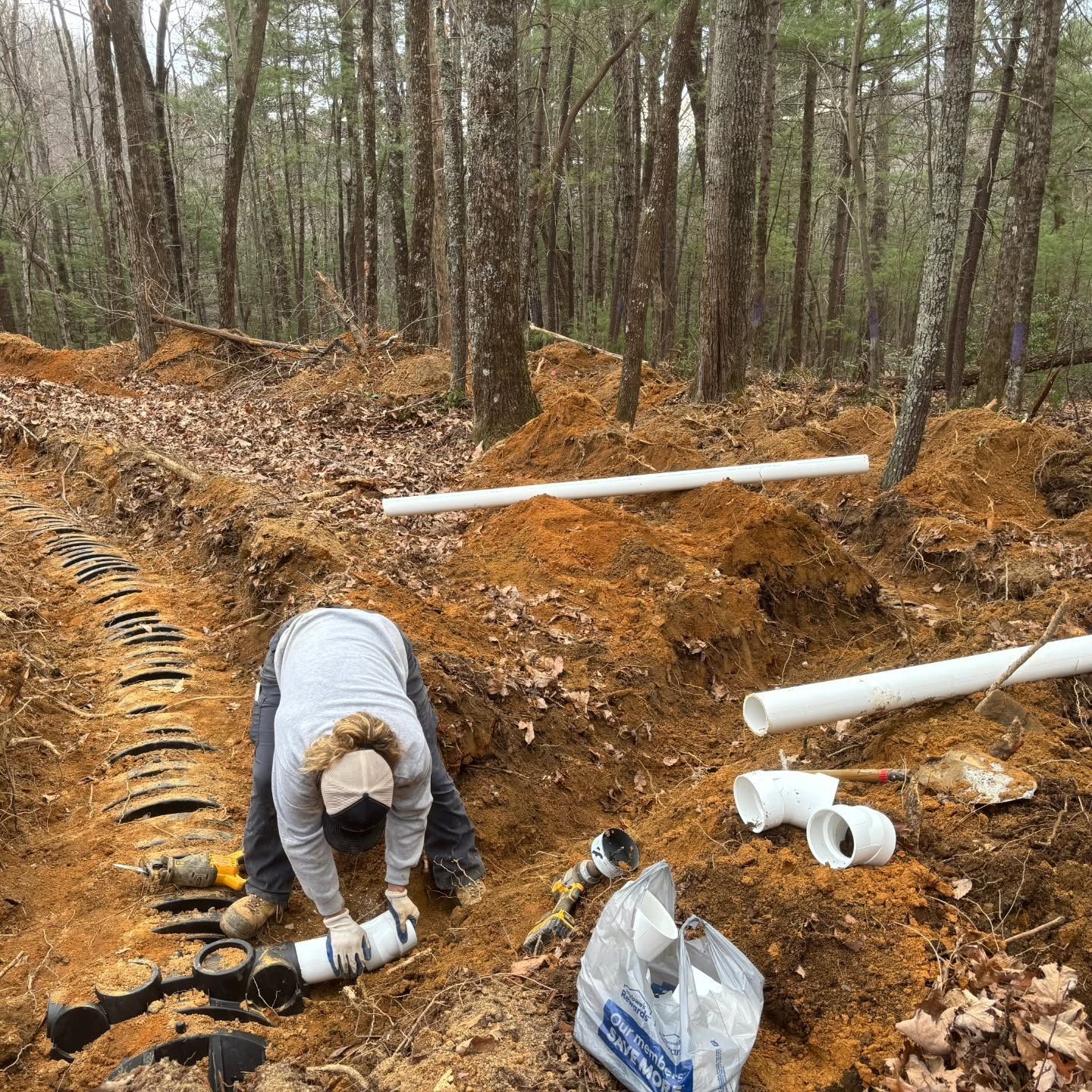 Person working with white PVC pipes at a muddy forest construction site
