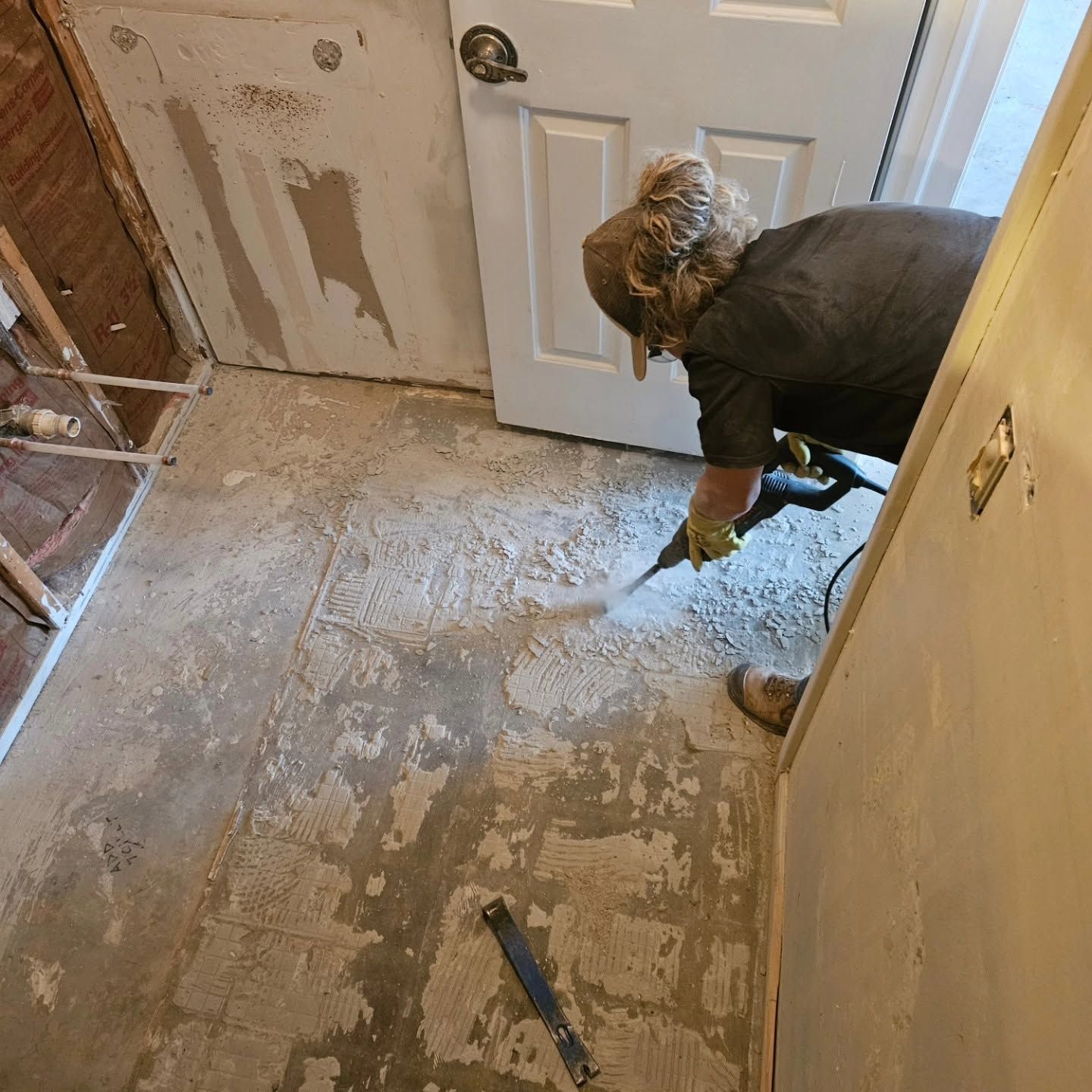 Person scraping old paint from a hallway floor during renovation.