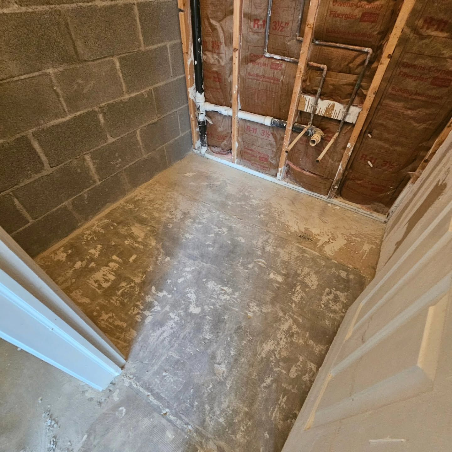 Small unfinished room with exposed studs, cinder block wall, and bare concrete floor viewed through a doorway
