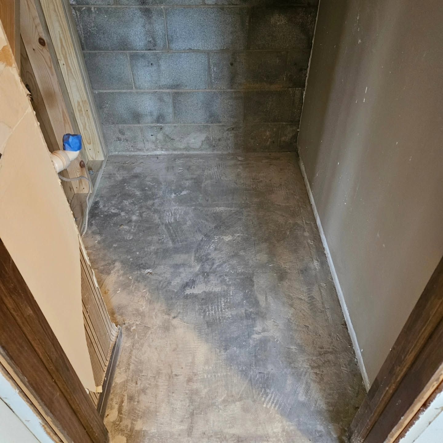 Narrow unfinished basement storage area with concrete floor and cinder block back wall