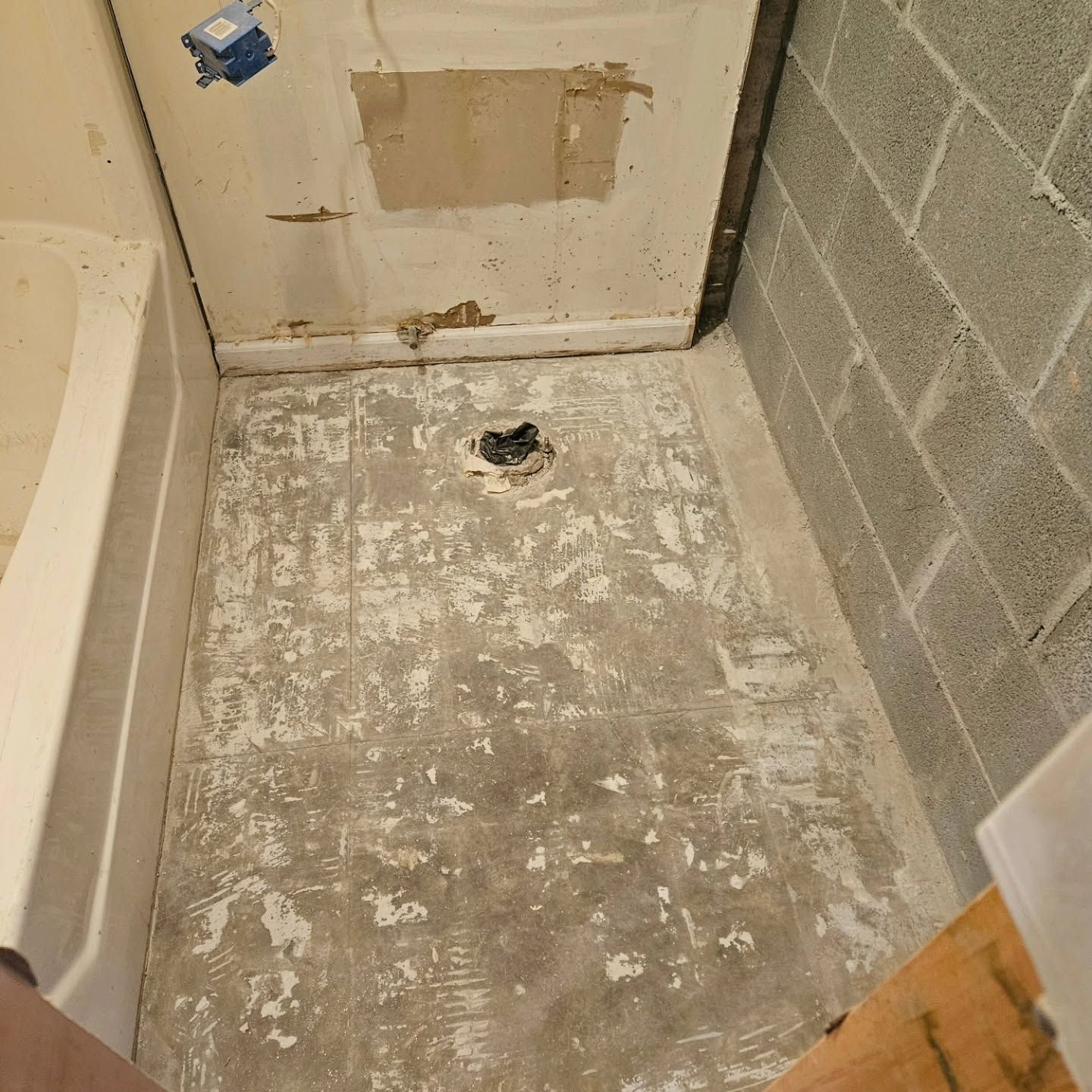 Small unfinished bathroom with bare concrete floor, drain, patched door, and cinder block wall.