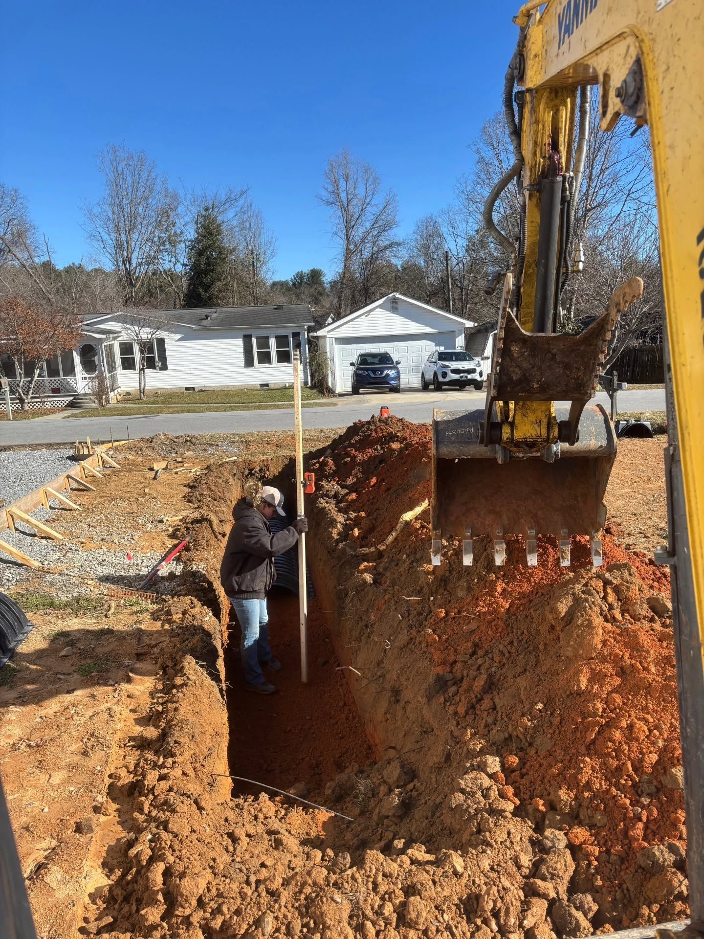 Worker in a trench beside an excavator at a residential construction site