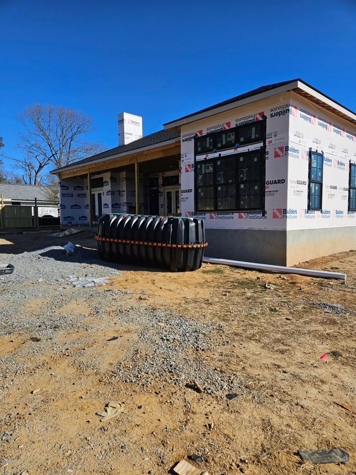 Partially built house with white exterior, black windows, and construction materials in front under a blue sky