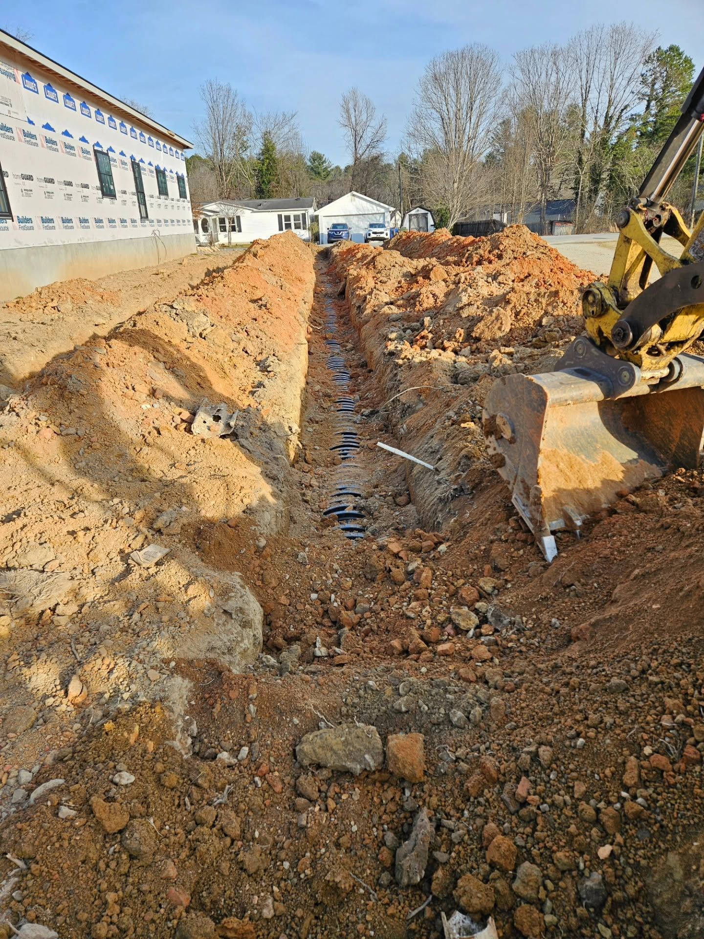 Excavator digging a deep trench beside a building on a muddy construction site