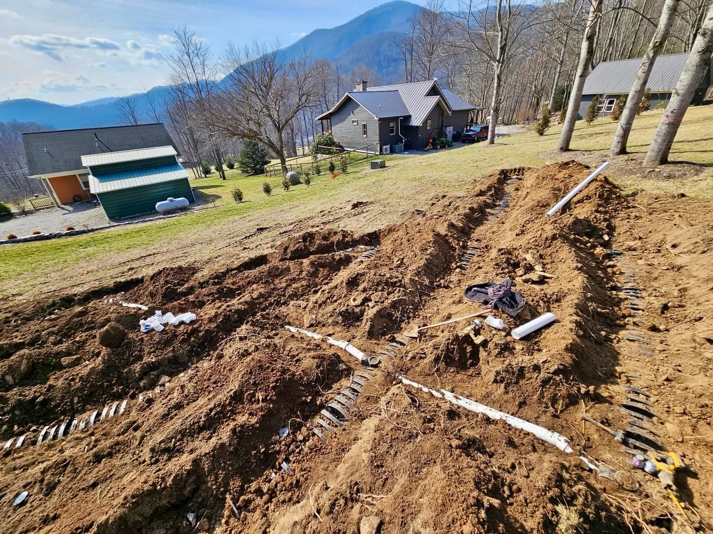 Freshly tilled brown field with white markers, rural houses, and mountains in the background