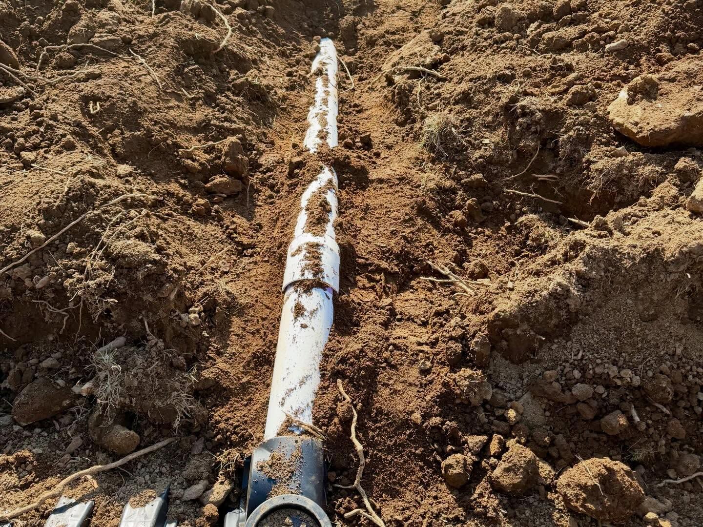 White pipe or cable partly buried in brown dirt, extending diagonally through a dug trench.